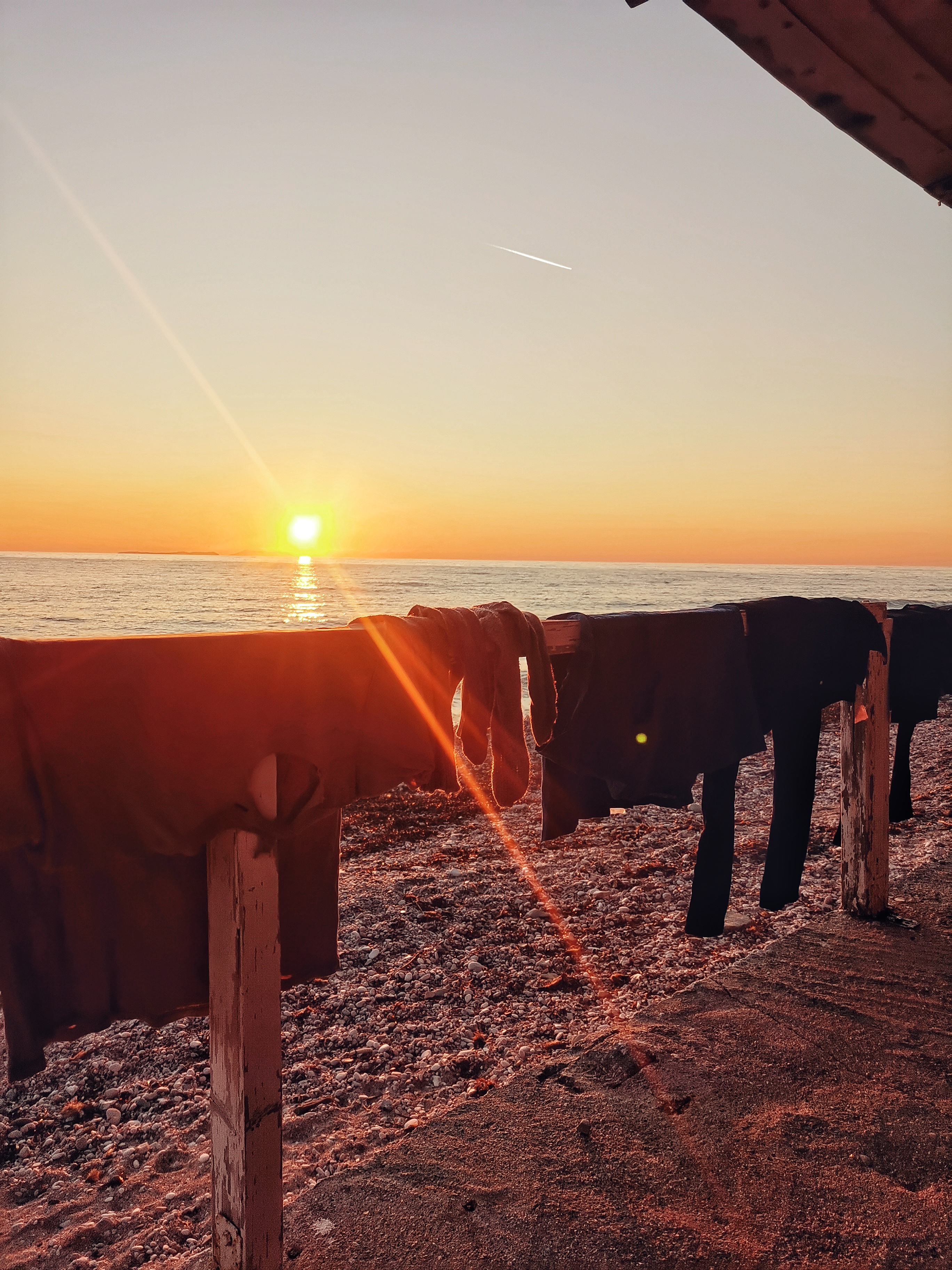 Trocknende Wäsche auf einem Geländer, im Hintergrund farbenfroher Sonnenuntergang über dem Meer