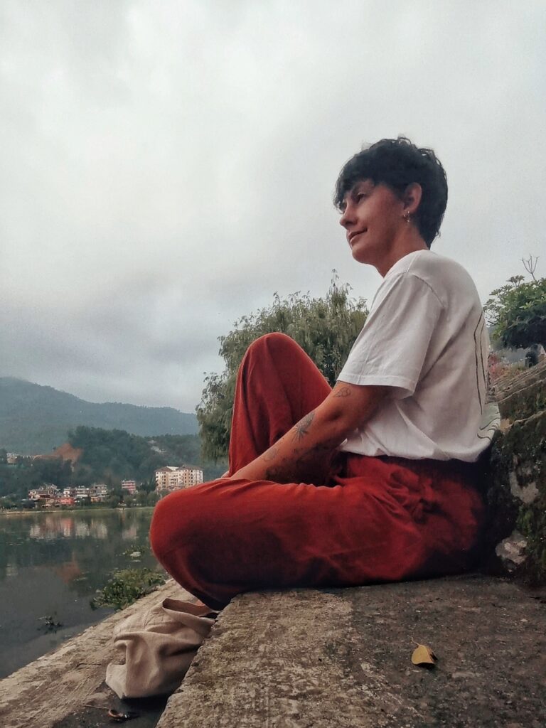 Ich sitze auf einer Steintreppe am See, in rostroter Leinenhose und weißem T-Shirt